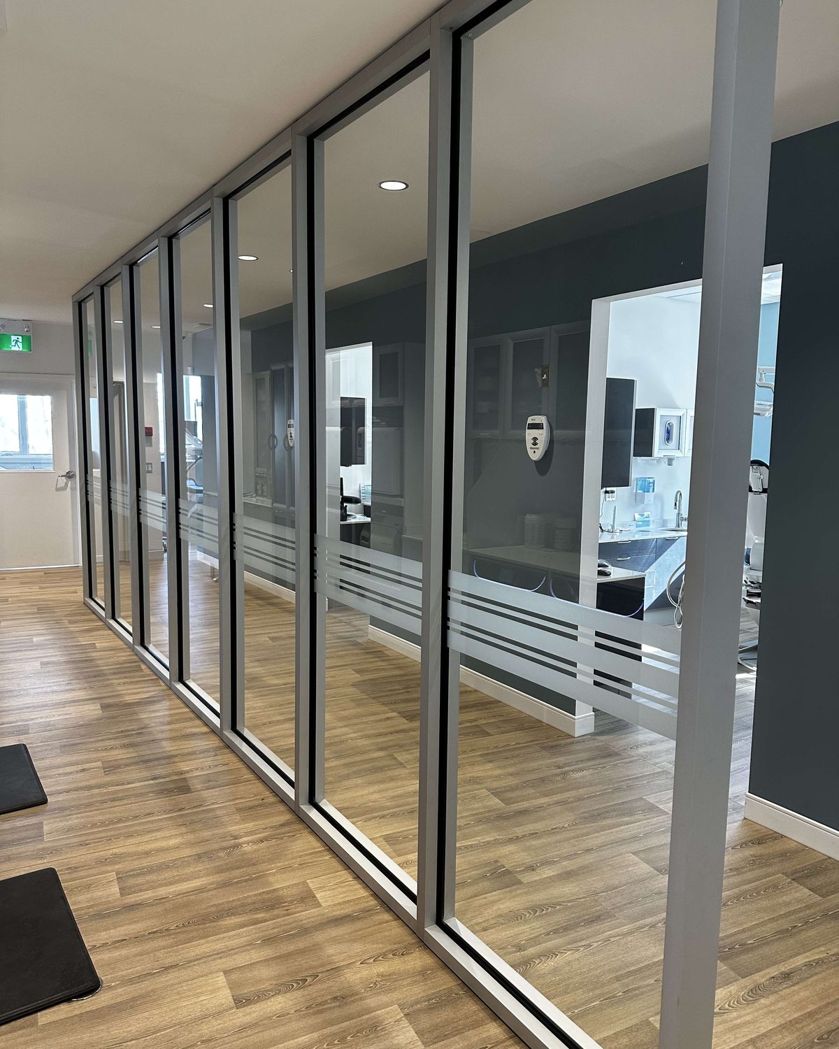 A corridor inside the Shelburne Dental clinic lined with floor-to-ceiling glass and aluminum frames, with frosted bands across the glass