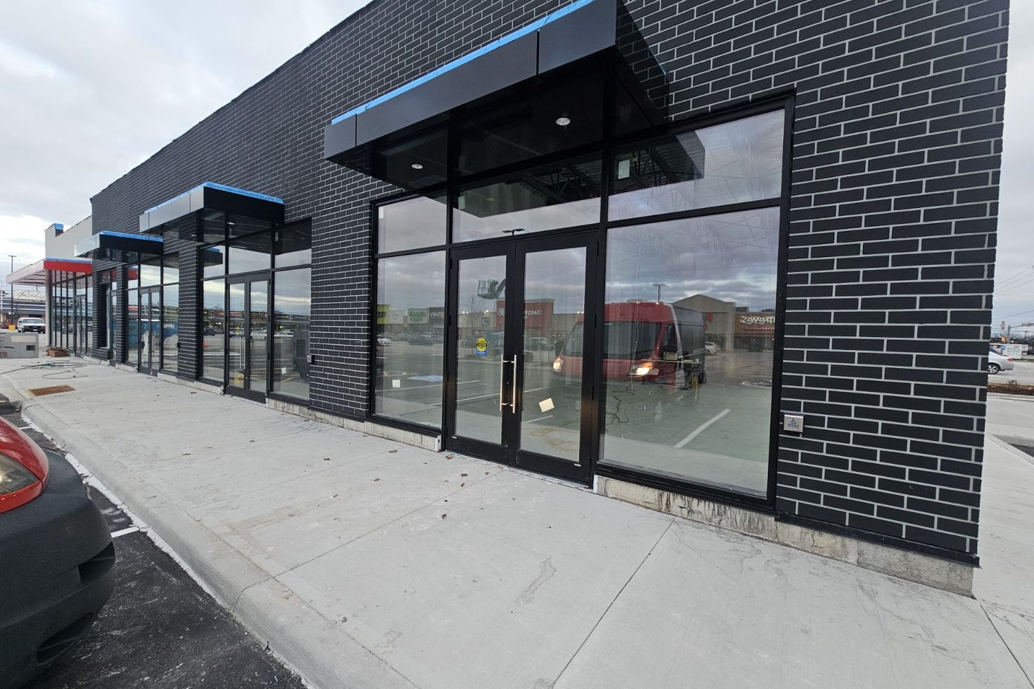 A glazed aluminum entrance with double doors under a dark metal canopy on the brick front of the new plaza building at 286 Bunting Road, St. Catharines