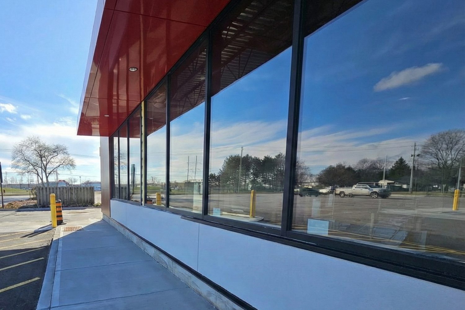 Tall tinted storefront windows in dark aluminum framing below a red fascia on the new plaza building at 286 Bunting Road, St. Catharines