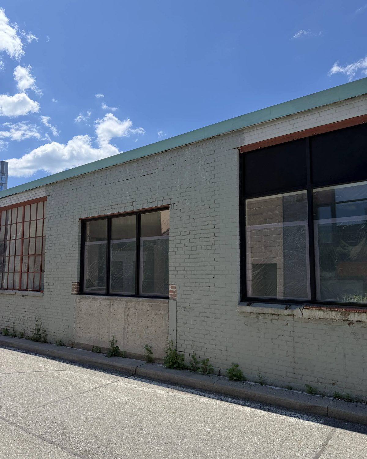 A run of new black-framed aluminum windows along the painted brick side elevation of a two-storey Toronto building, installed by Canuck Door Systems