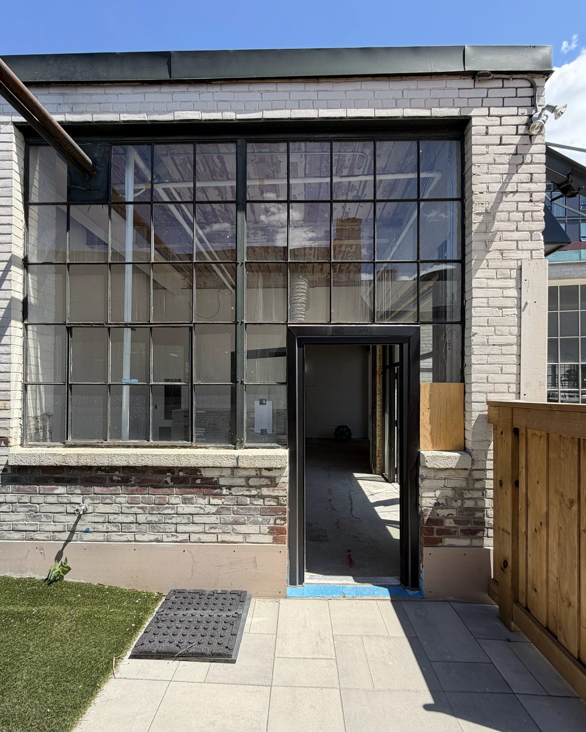 A multi-lite glazed screen in black aluminum framing at the rear of a Toronto brick building, with a new black-framed door opening onto a paved patio, installed by Canuck Door Systems