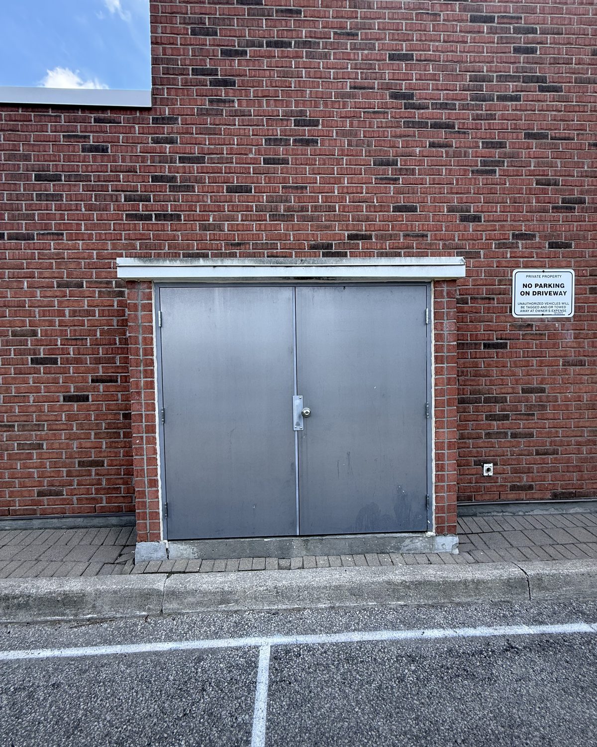 A pair of grey hollow metal doors with a lever handle, under a white head flashing in a red brick wall