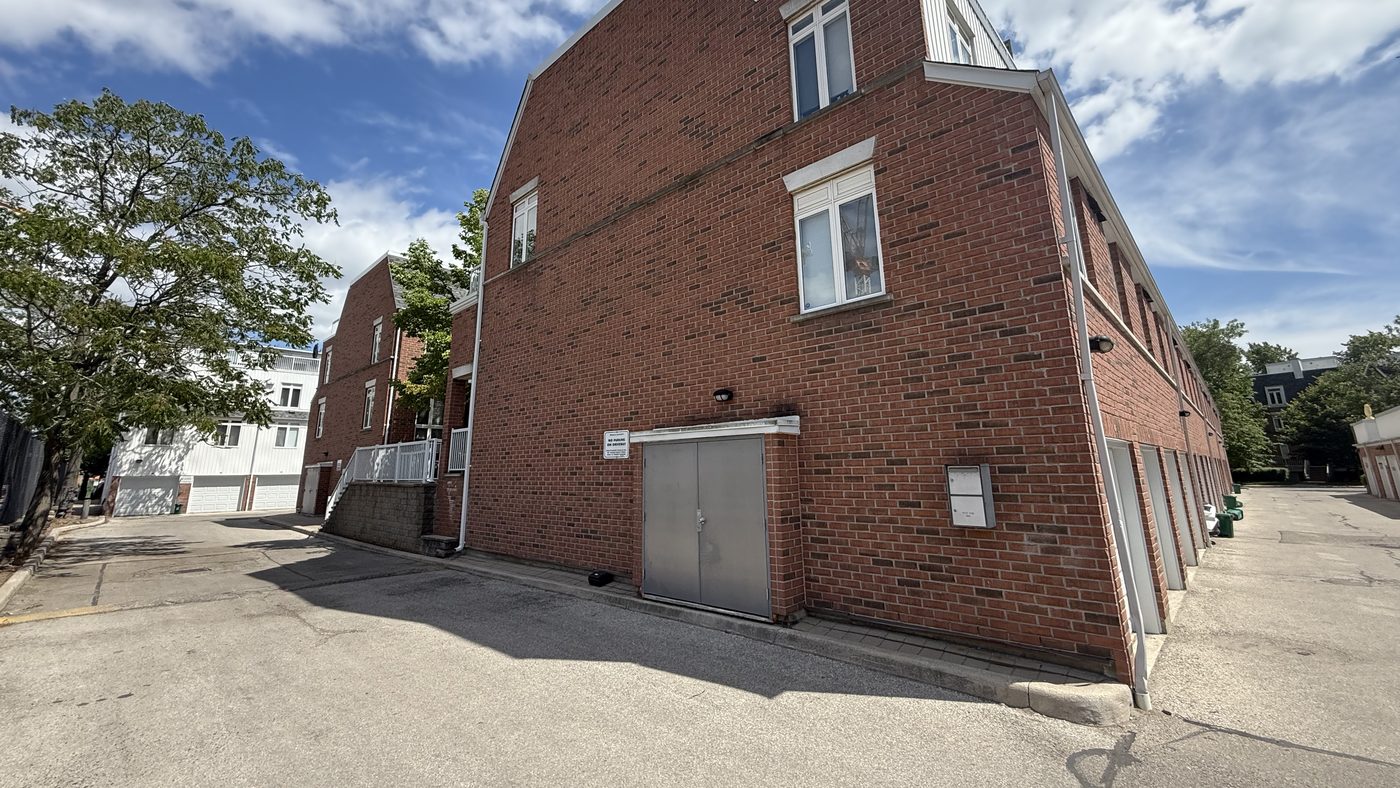 A red brick townhome building in downtown Toronto, with a new pair of grey metal doors at the base of an end wall beside a laneway