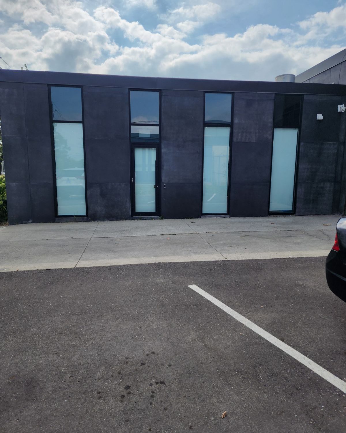 Tall narrow aluminum-framed glazing and an entrance door in the dark facade of the Smoke Arsenal building in Toronto, seen from the parking lot