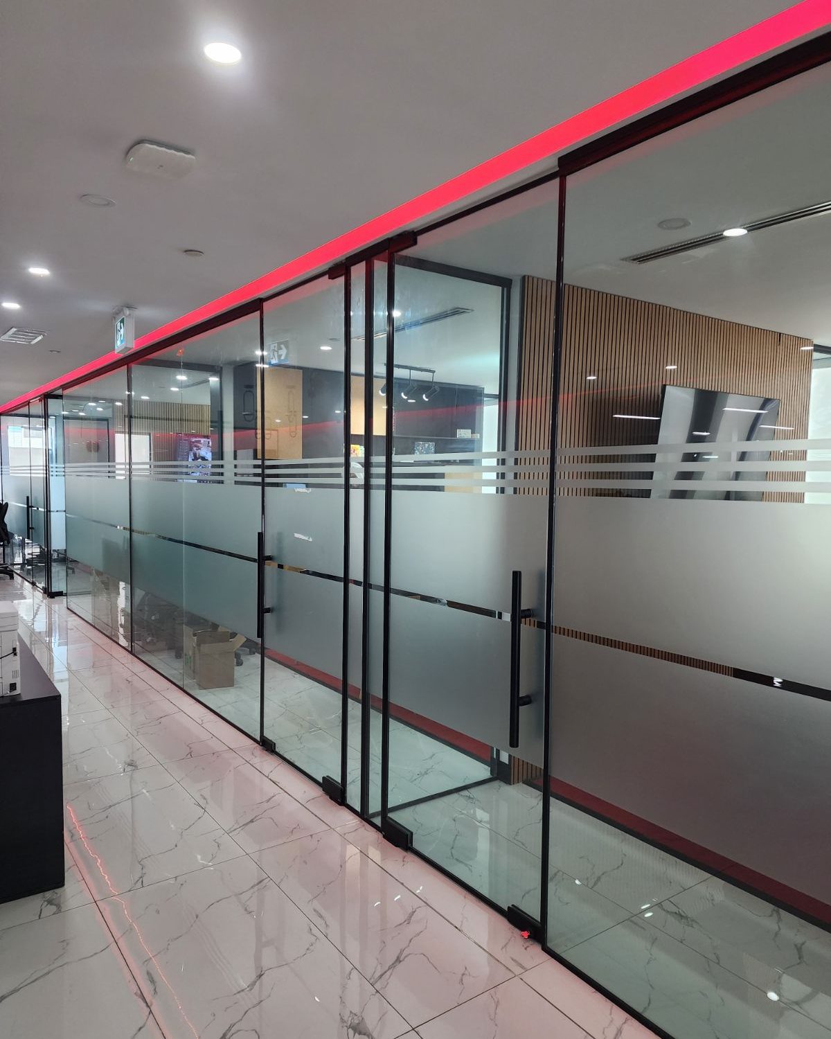 A long run of frameless glass office partitions with frosted privacy bands along a corridor inside the Smoke Arsenal office in Toronto
