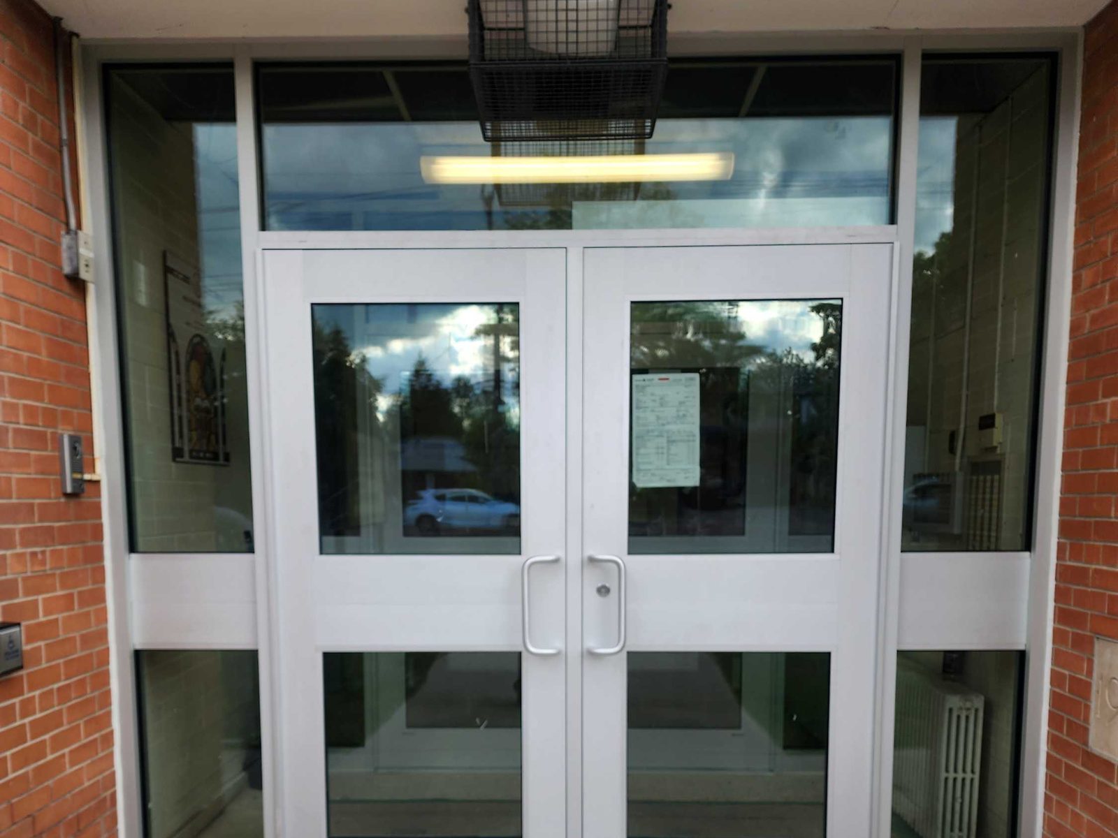 A new clear anodized aluminum double-door entrance with glazed sidelites and a glazed transom, set into the red brick of St. Albert Catholic School in Toronto, installed by Canuck Door Systems