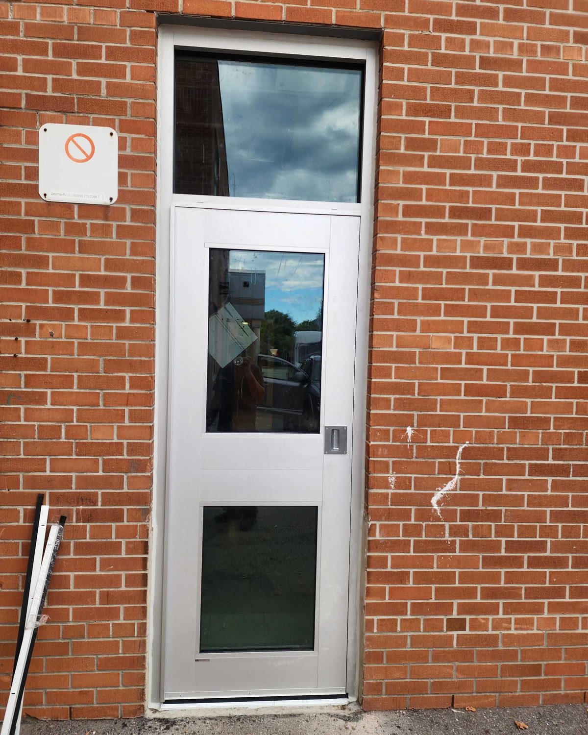 A narrow single door in a red brick wall at St. Albert Catholic School, with glazed lites in the door and a glazed transom above it
