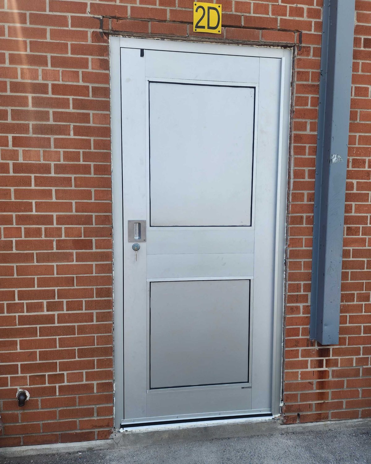 A single aluminum-framed door in a red brick wall at St. Albert Catholic School, filled with flat insulated metal panels instead of glass