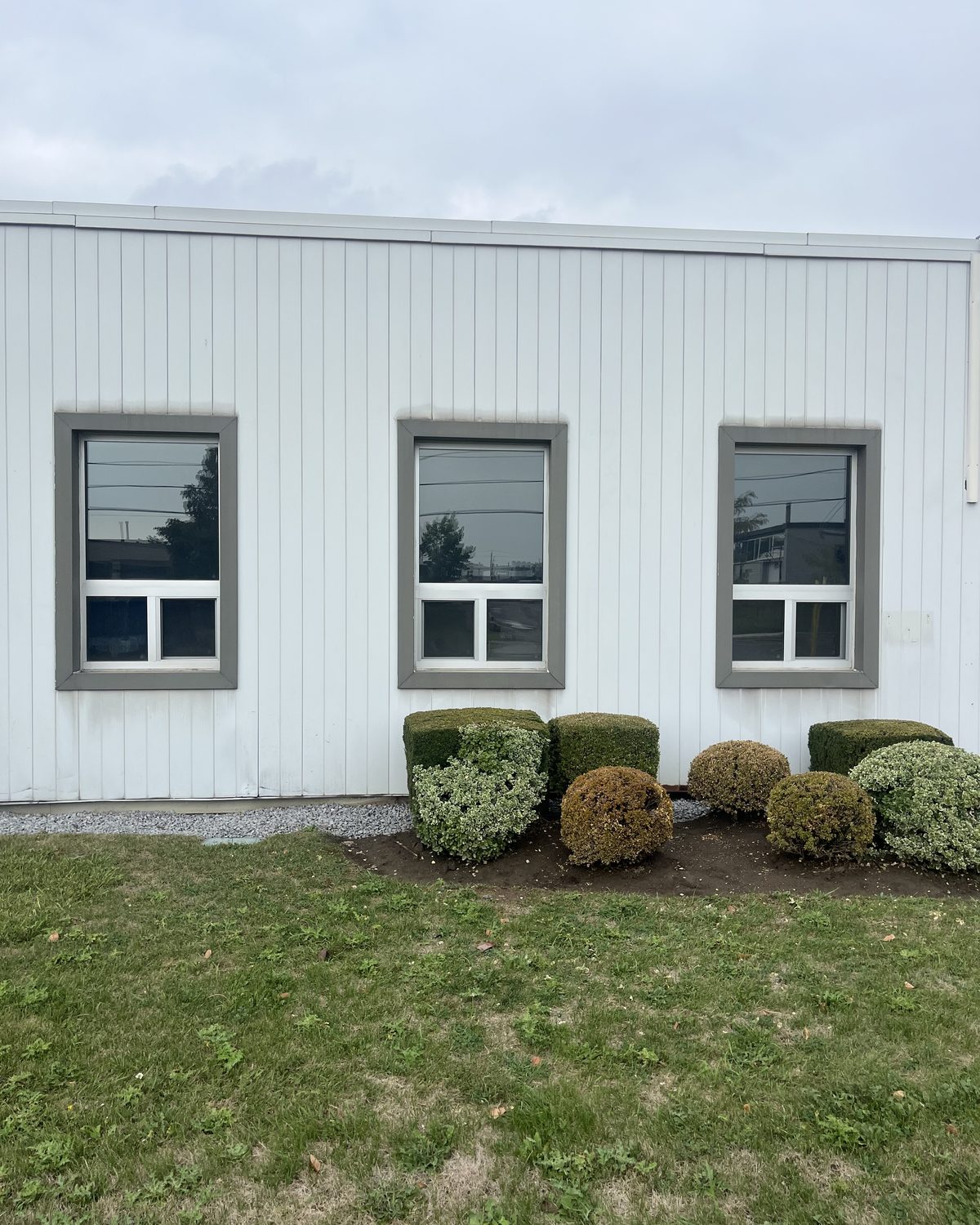 Three new clear anodized aluminum sliding windows in grey surrounds on the white-clad side wall of a commercial building on Sunrise Avenue, Toronto