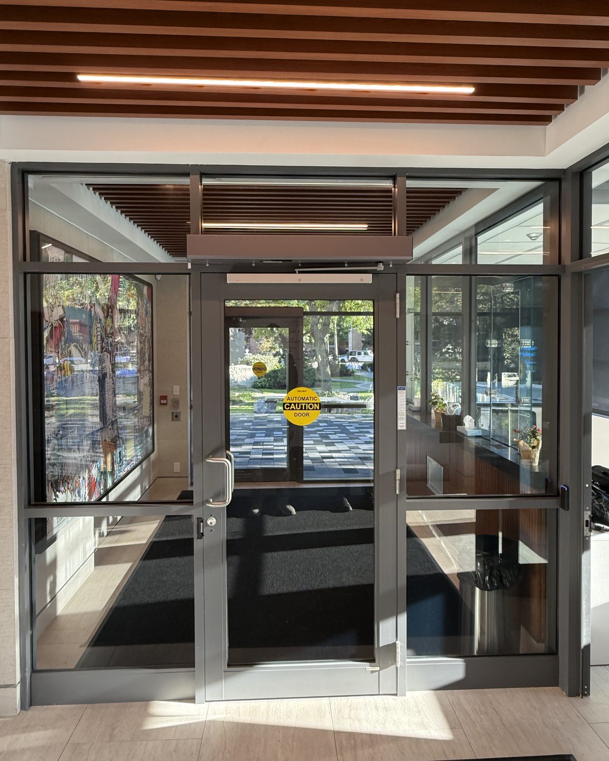 Grey aluminum vestibule doors with glass inside the west entrance at Temple Sinai Congregation in Toronto, under a wood-slat ceiling