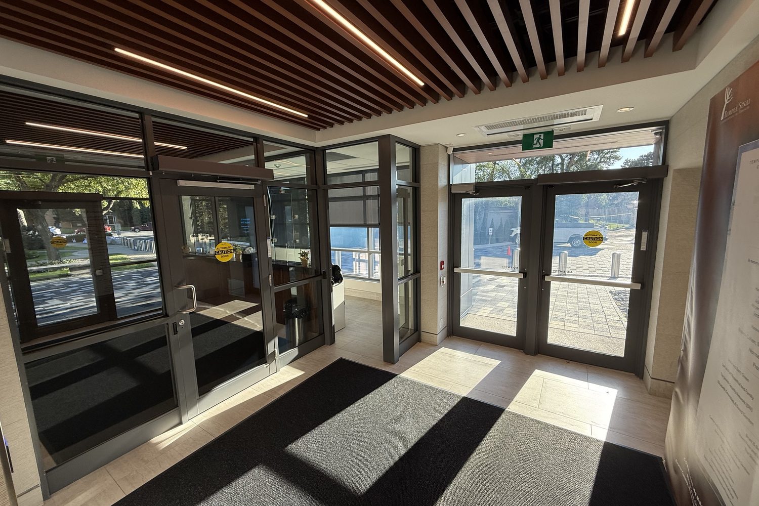 Inside the new glazed vestibule at Temple Sinai Congregation in Toronto, looking through grey aluminum-framed glass walls and doors to the outside