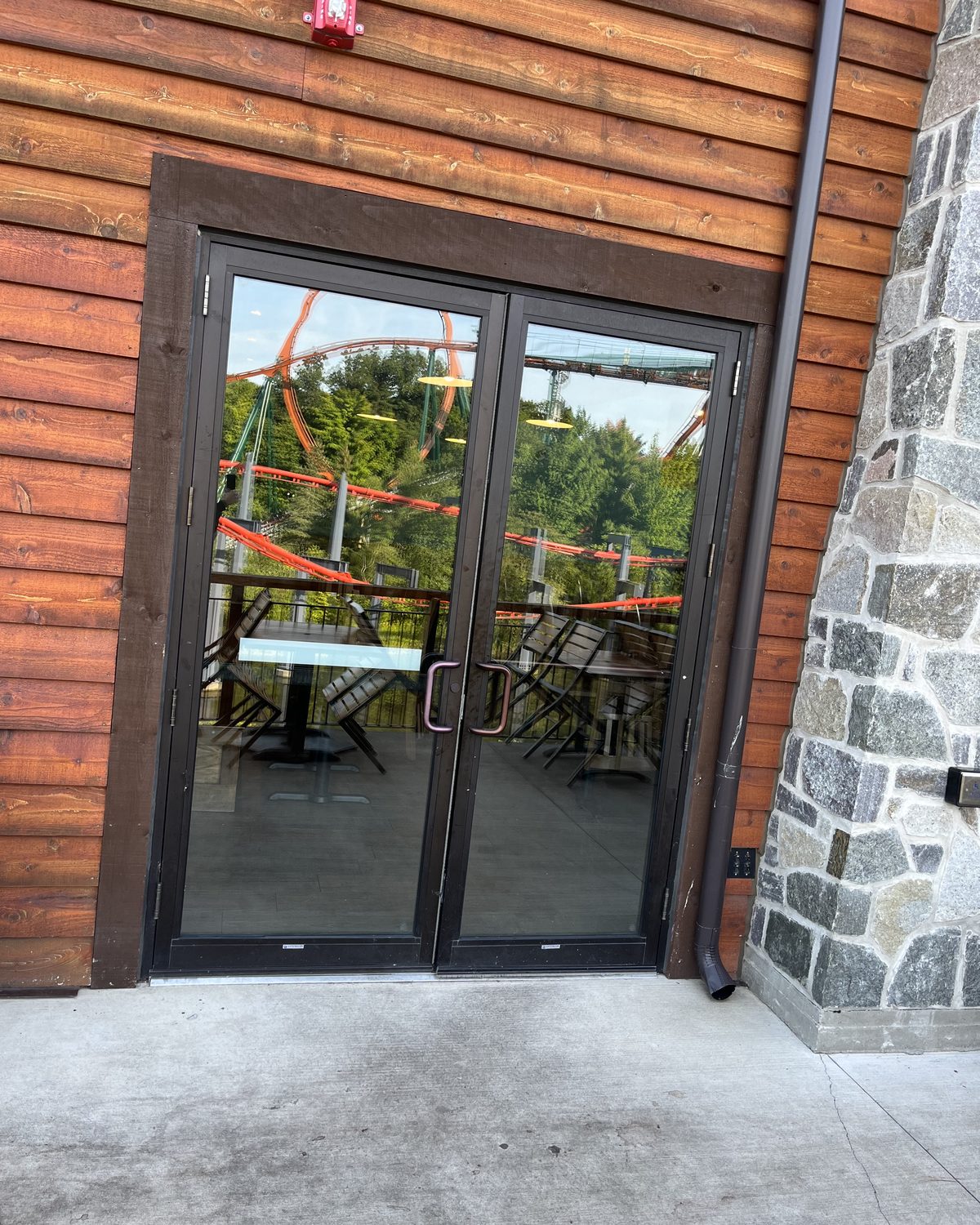 A pair of dark aluminum glass entrance doors set into the timber cladding of Lazy Bear Lodge, beside a stone pier