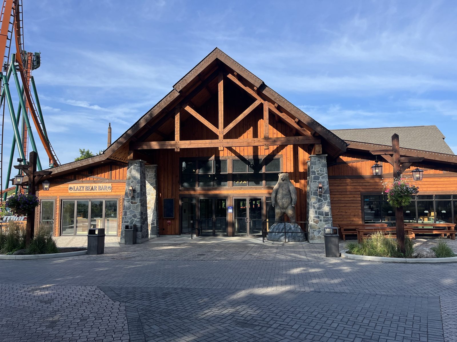 Lazy Bear Lodge at Canada's Wonderland in Vaughan, a timber-framed restaurant with a tall glazed gable and aluminum storefront glazing along its front, with a roller coaster behind