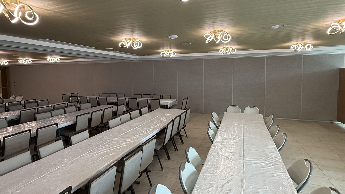 A large school hall in Vaughan set with long tables and chairs, with a closed operable wall of grey carpeted panels forming the back wall of the room
