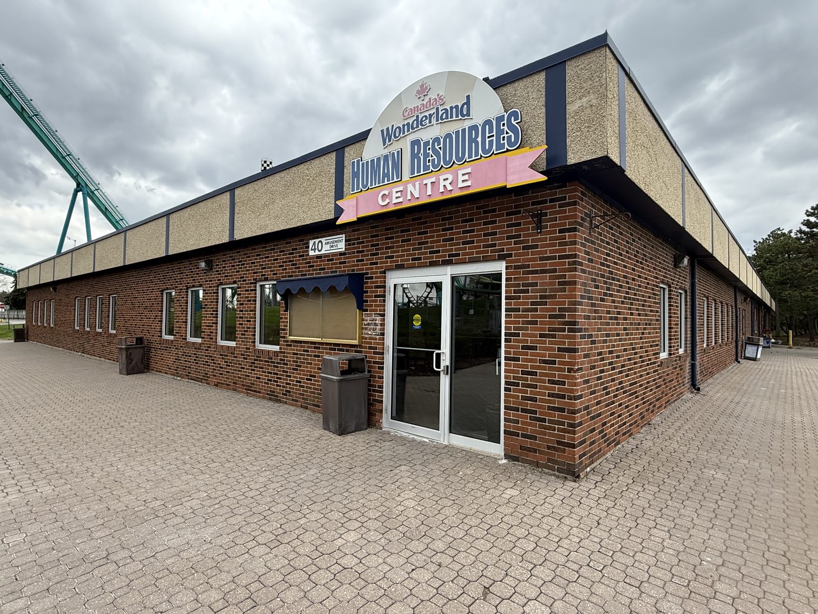 A clear anodized aluminum glass entrance door with a matching sidelite in the brick wall of a long single-storey building at Canada's Wonderland in Vaughan, with new windows along the same wall, installed by Canuck Door Systems