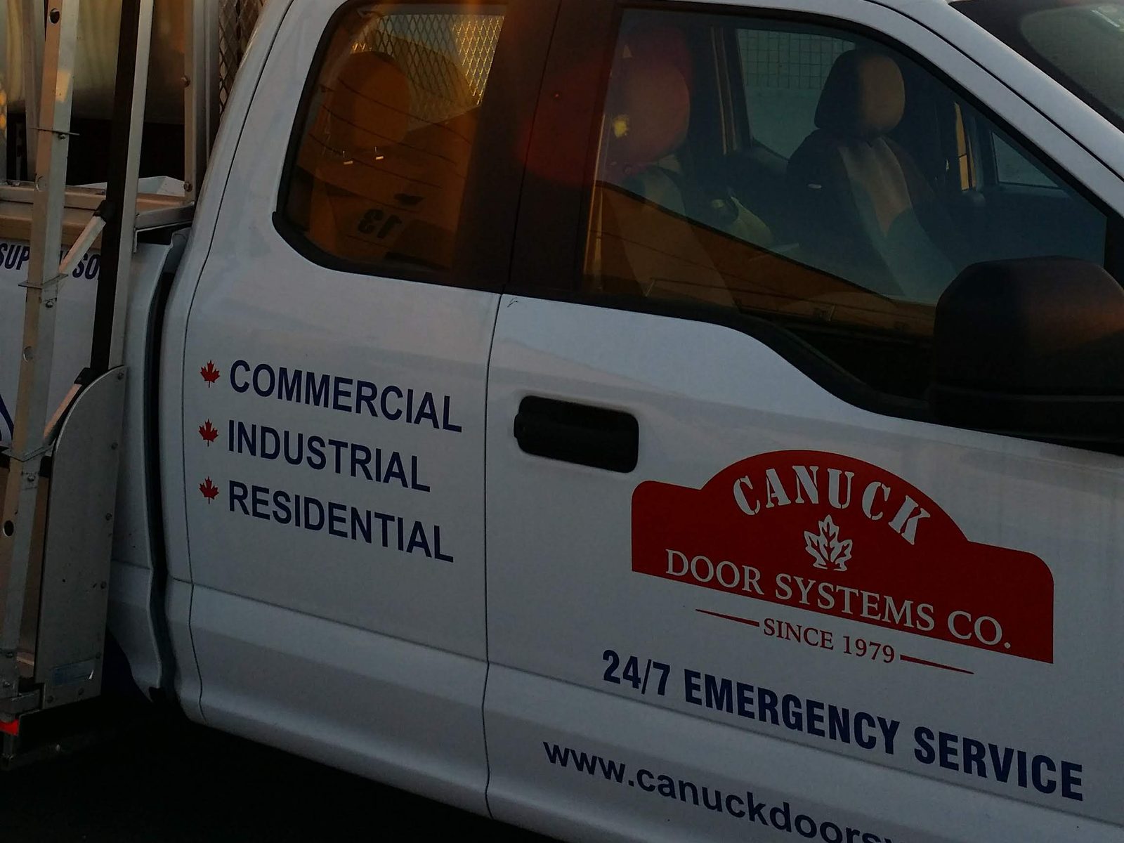A Canuck Door Systems service truck with a glass rack, signwritten commercial, industrial, residential and 24/7 emergency service, parked at first light