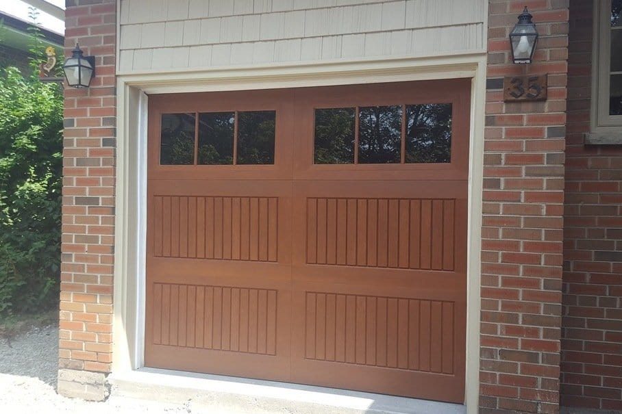A woodgrain fibreglass garage door with a glazed top section, closed in a brick opening with a coach light beside it