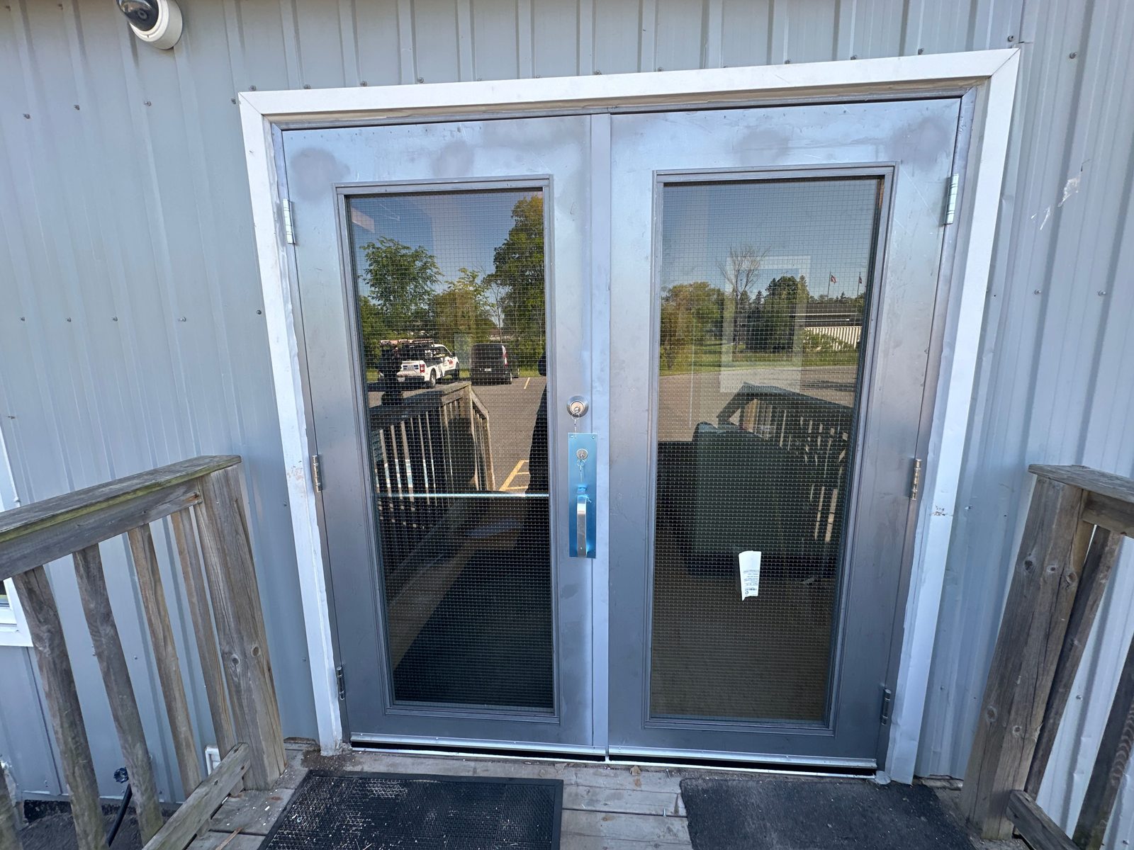 Stainless steel double doors with wired-glass lites, newly installed at the entrance of a steel-clad commercial building