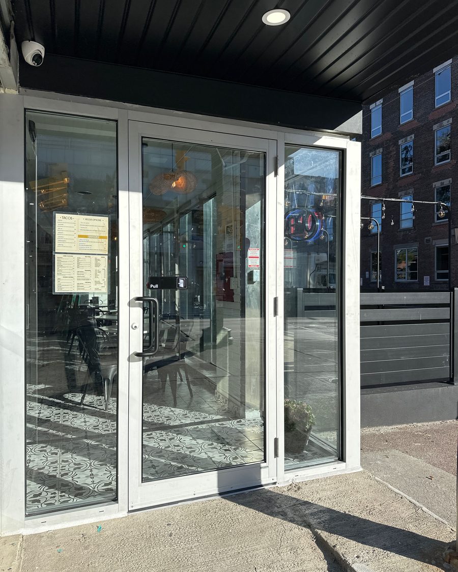 A silver aluminum storefront entrance under a dark soffit: a single glass door with a pull handle and a "Pull" sign, between two full-height fixed glass sidelites, with a restaurant's tiled floor visible through the glass