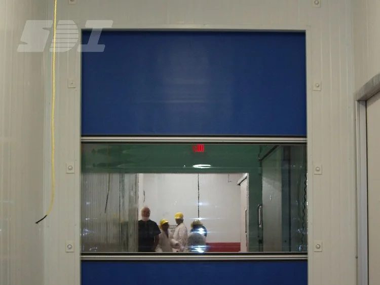 A blue high-speed fabric door with a full-width vision panel, closed across an opening in a food plant — an SDI product photograph of the type of door we supply and service