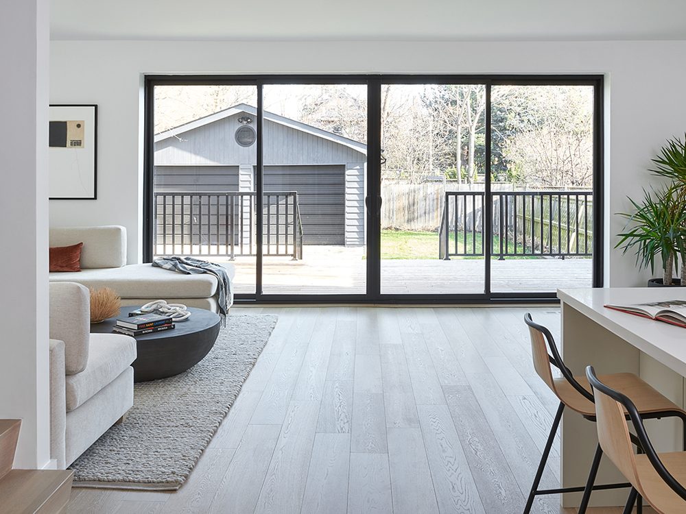 A wide black-framed four-panel sliding patio door across the back wall of a living room, opening onto a wooden deck